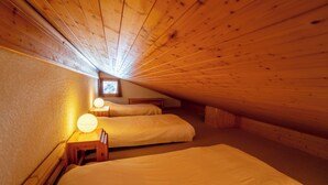 Ein gemütliches Schlafzimmer im Dachgeschoss mit zwei Betten und Holz-Kopfteilen, mit geneigter Decke.