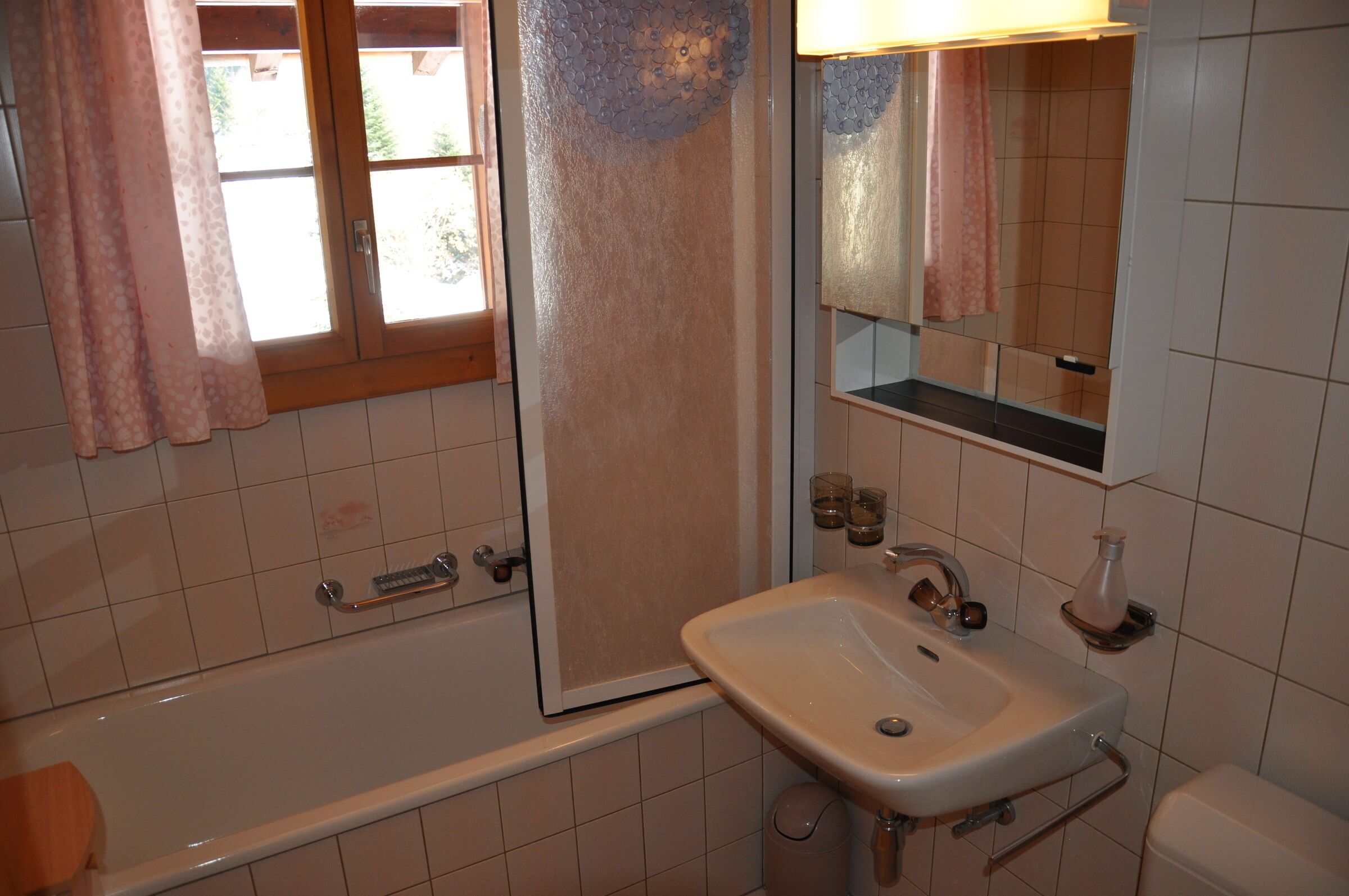 A bathroom with a bathtub, a sink, a mirror, and a window with curtains.