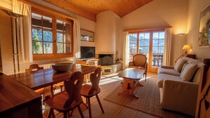 Ein gemütliches Wohnzimmer mit Kamin, Holzmöbeln und großen Fenstern mit Blick auf die Berge.