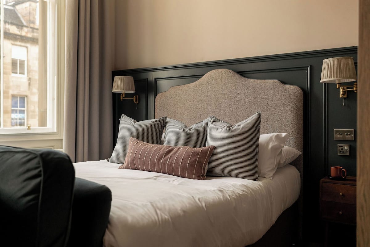 A neatly made bed with striped and solid pillows, a dark headboard, and two wall-mounted lamps.