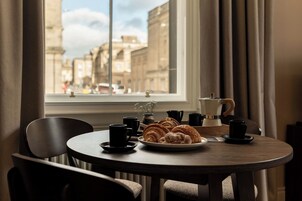 A round table with a plate of croissants, a coffee maker, and several black cups.