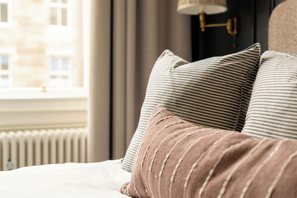 A bed with striped pillows and a brown pillow, a window with curtains, and a radiator. - Moment George IV Bridge (Edinburgh)
