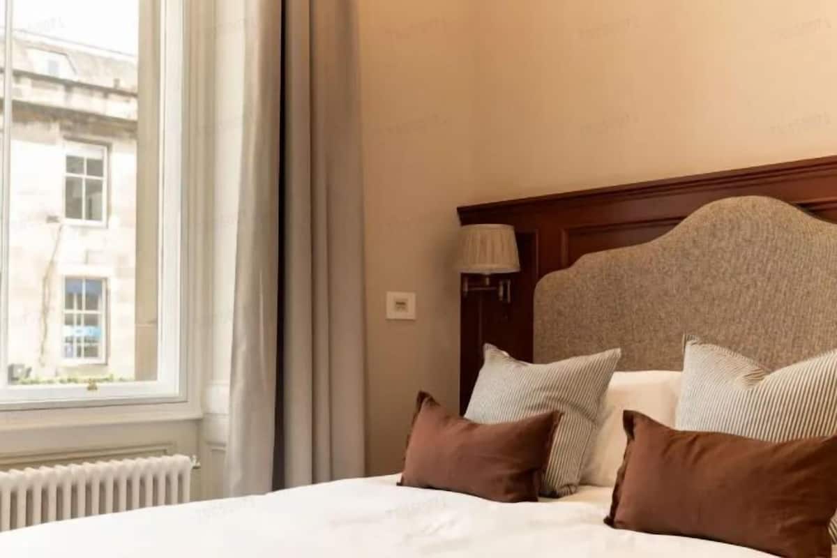 A hotel room with a large window, a bed with white bedding, and a wooden headboard.