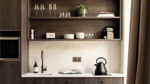 A modern kitchen with dark wood cabinetry, a marble countertop, and a built-in shelf above the sink holding glasses, a plant, and books. - Moment George IV Bridge (Edinburgh)