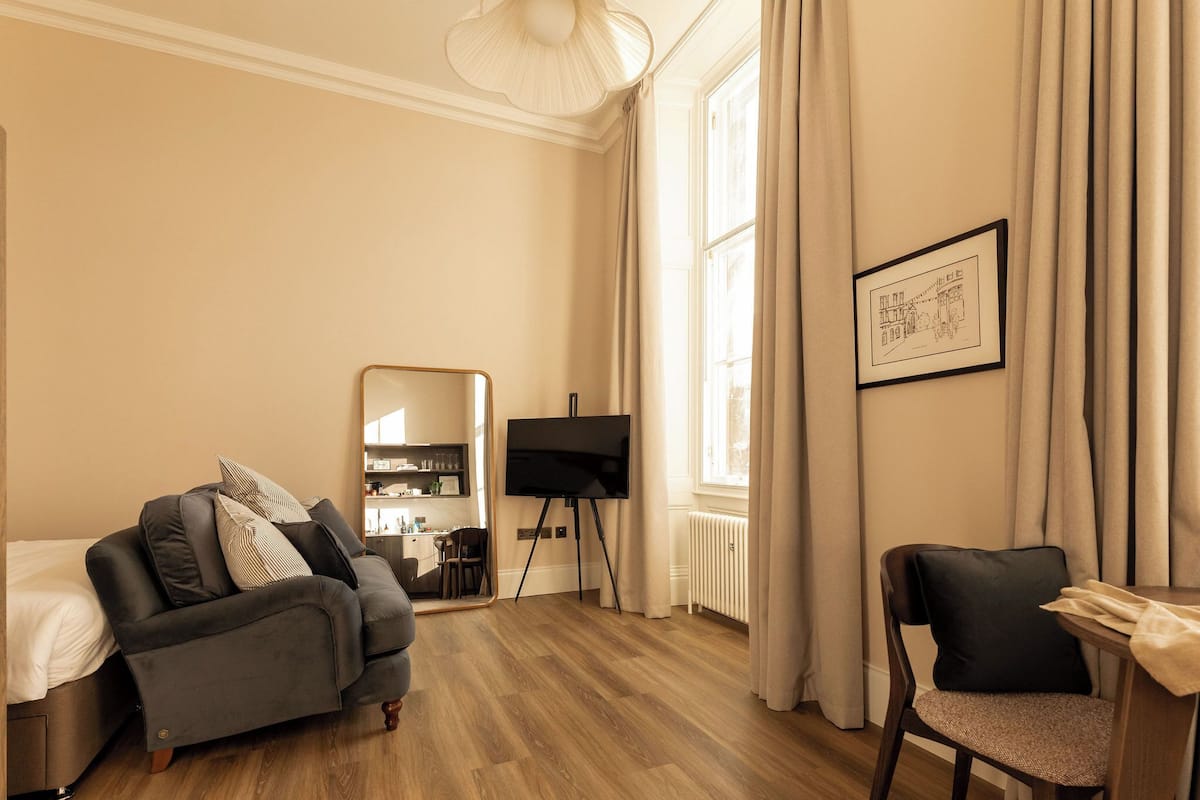 A modern living room with a sofa, a chair, a TV on a stand, and a framed picture on the wall.