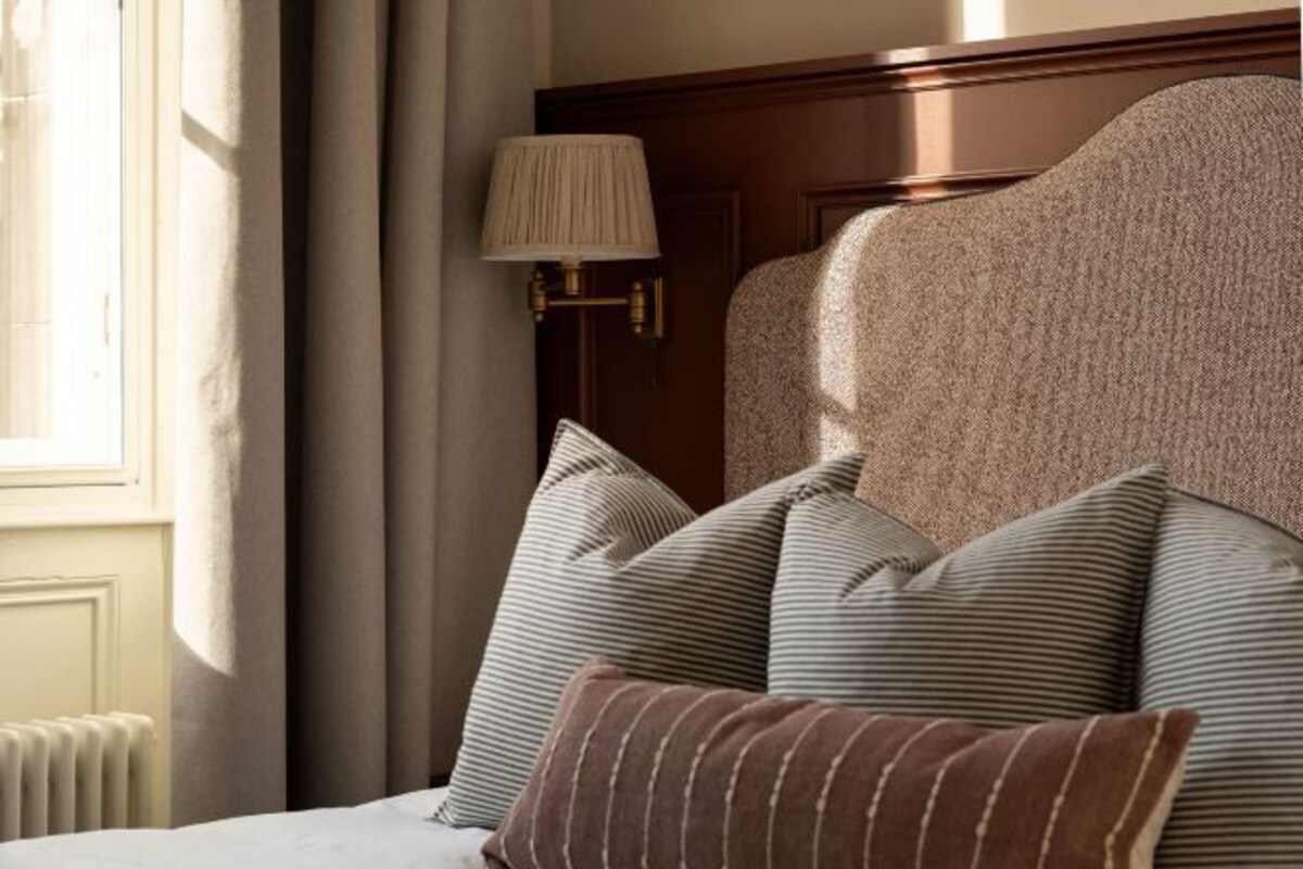 A hotel room with a bed, striped pillows, a lamp, and a window with curtains.