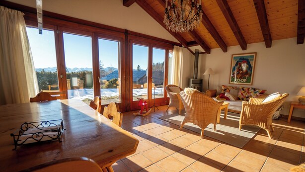 Un salón espacioso con una mesa de comedor de madera, sillas de mimbre y un amplio ventanal con vistas a las montañas.
