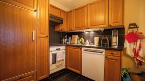 A kitchen with wooden cabinets, a stove, a dishwasher, and various kitchen items on the countertop. - The flat is located above the village of Gryon, in Les Verneys Soleil, 2 km from the Fracherets ski (Gryon)