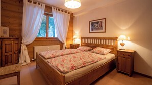 A wooden room with a bed, two bedside tables with lamps, a window with curtains, and a framed picture on the wall. - The flat is located above the village of Gryon, in Les Verneys Soleil, 2 km from the Fracherets ski (Gryon)