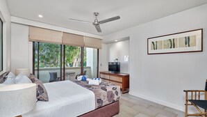 Ein modernes Hotelzimmer mit einem großen Bett, einem Deckenventilator, einem Fernseher und einem Fenster mit Blick auf Grünflächen.