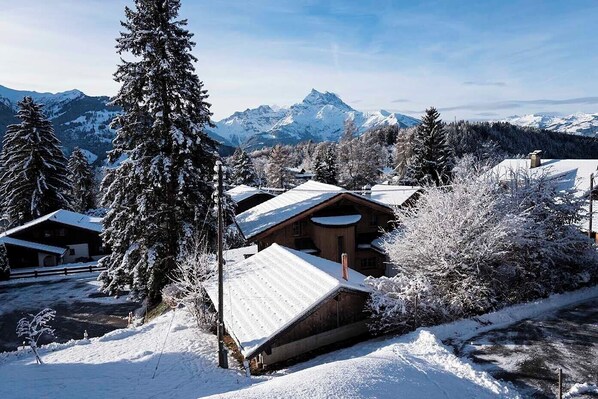 Un albergue cubierto de nieve con cabañas de madera, rodeado de árboles cargados de nieve y montañas al fondo.