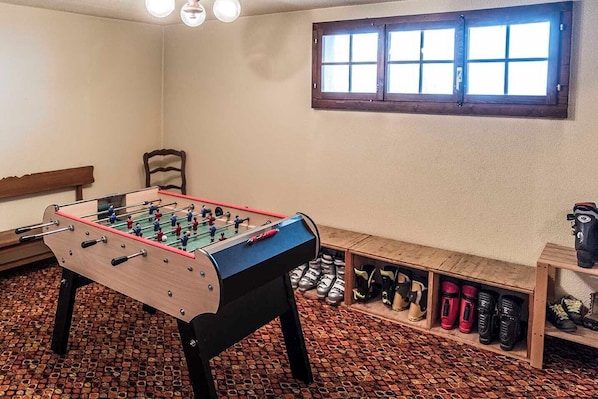 A room with a foosball table, a bench, a shoe rack, and a window with blinds.