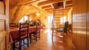 A cozy attic room with wooden beams, a dining table with chairs, a ladder, and a green armchair.
