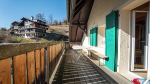 A wooden deck with a bench and a table, overlooking a hillside with a large building.