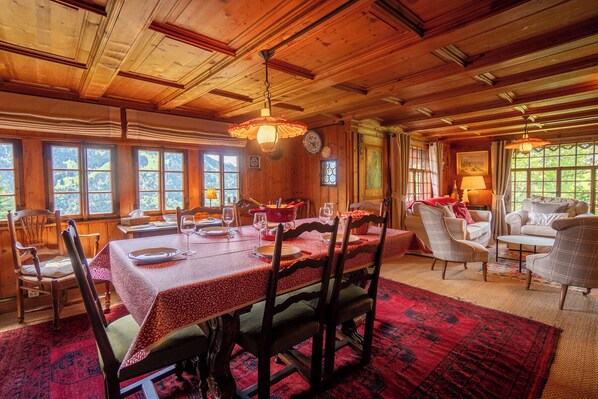 Un comedor de madera con una gran mesa dispuesta para seis personas, rodeada de sillas. Hay un sofá y una mesa de centro en el área de estar contigua.