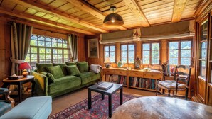A cozy cabin interior with a green sofa, wooden desk, and a large window overlooking greenery. - This beautiful chalet built in 1872 is located in the heart of the pretty village of Gryon. Gryon tr (Gryon)