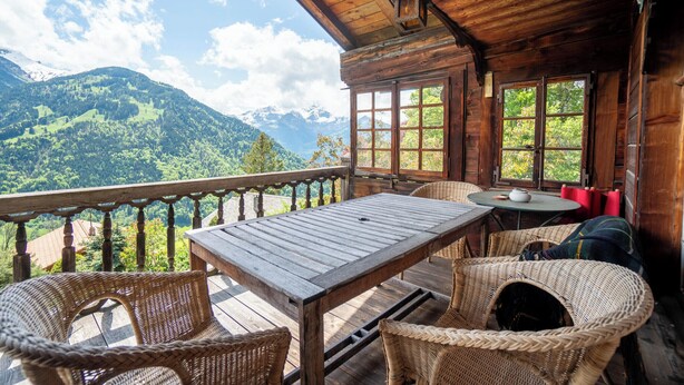 A wooden deck with wicker furniture, a table, and chairs, overlooking a mountainous landscape. - This beautiful chalet built in 1872 is located in the heart of the pretty village of Gryon. Gryon tr (Gryon)