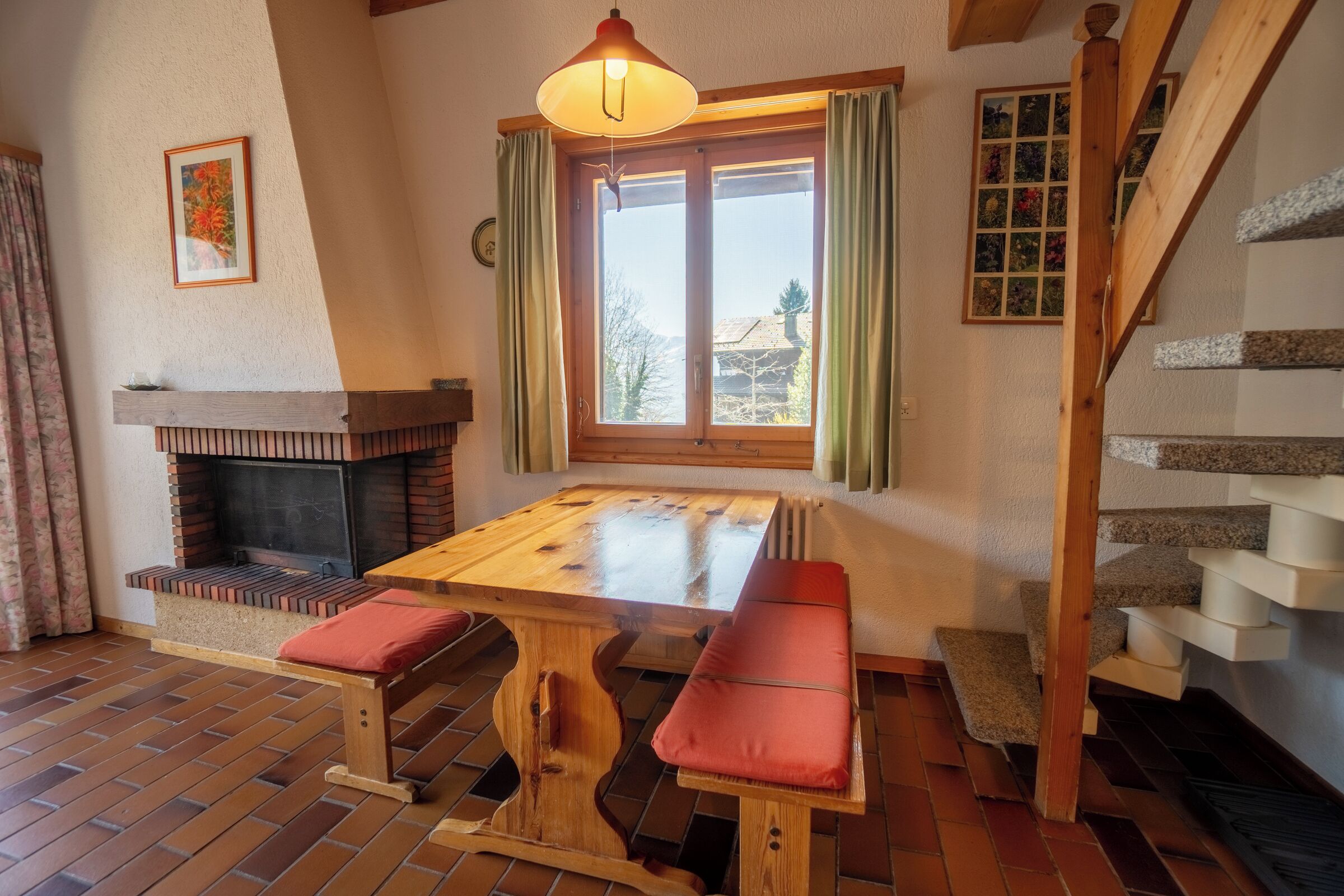 A cozy room with a fireplace, wooden table, bench, and a staircase.