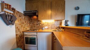 Una cocina compacta con armarios de madera, salpicadero de azulejos, estufa, lavavajillas y encimera de madera.