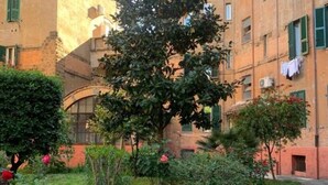 A courtyard with a large tree, a small garden, and a building with multiple windows and balconies. - Apartment within walking distance of the Vatican Museums. Central and served by transportation and metro (Roma)