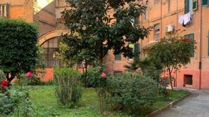 A courtyard with a paved path, lush greenery, and a building with red brick walls and green shutters. - Apartment within walking distance of the Vatican Museums. Central and served by transportation and metro (Roma)
