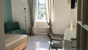 A small, well-lit room with a bed, a chair, a window with curtains, and a desk. - Apartment within walking distance of the Vatican Museums. Central and served by transportation and metro (Roma)