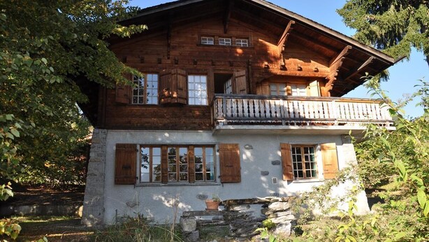 A rustic wooden chalet with a balcony, stone foundation, and wooden shutters.