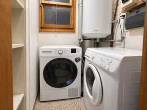 A compact laundry room with a front-loading washer and dryer, a window, and a water heater.