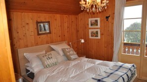 Un dormitorio con paneles de madera, una cama, una araña y una ventana con vistas.