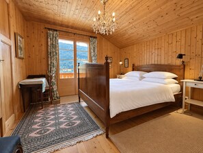 A wooden-paneled bedroom with a four-poster bed, a chandelier, and a view through a window.
