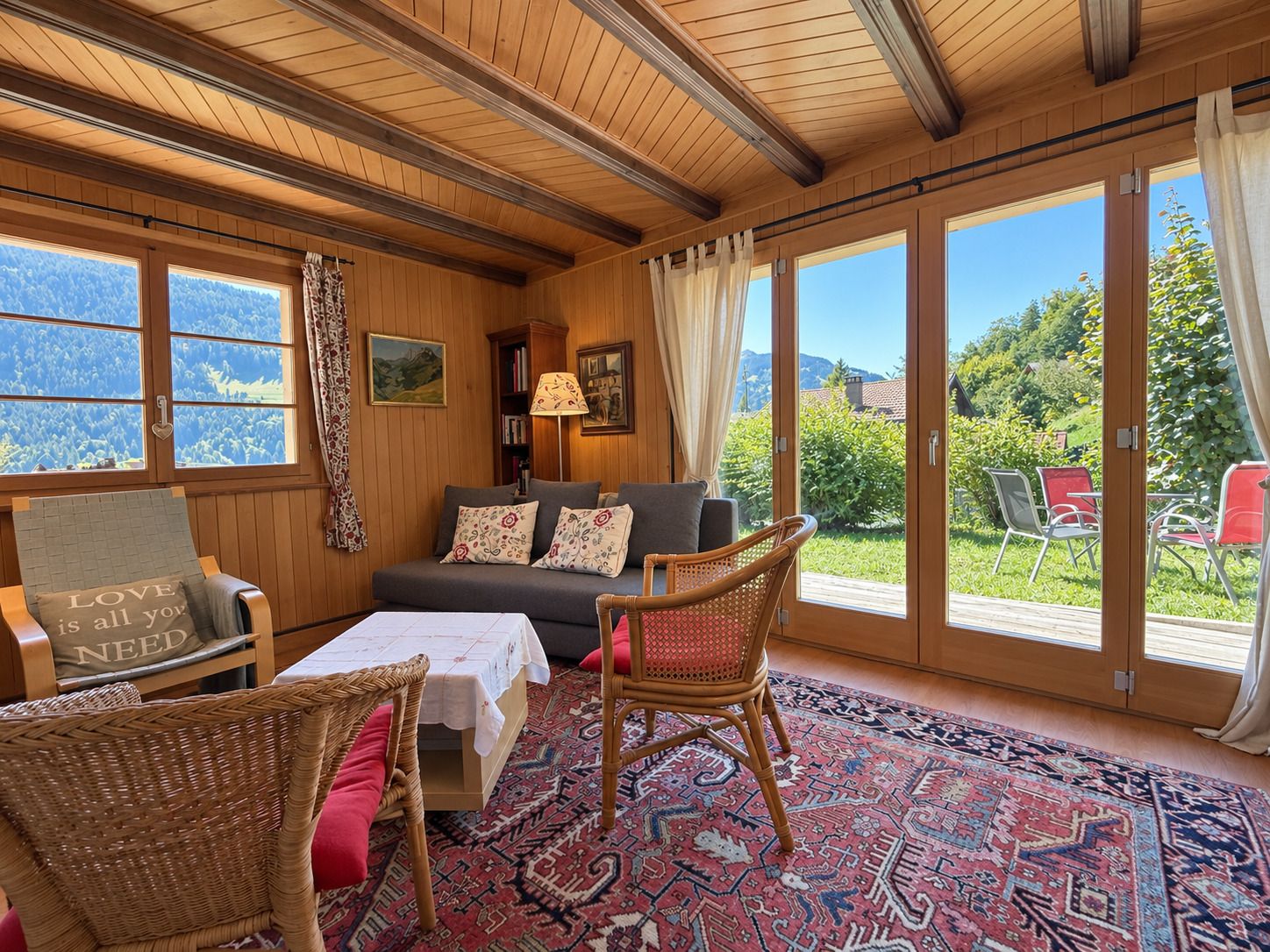 A cozy room with a sofa, chairs, a table, and a view of a garden through large windows.