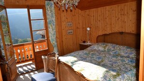 Una habitación con paneles de madera, una cama, una silla, una mesita de noche y una ventana con vistas a un edificio tradicional.
