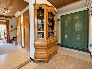 Un armario de madera con puertas de cristal, un guardarropa verde con tiradores decorativos y una escalera que lleva a otra habitación.