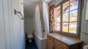 Un baño con bañera, inodoro y ventana con cortinas.