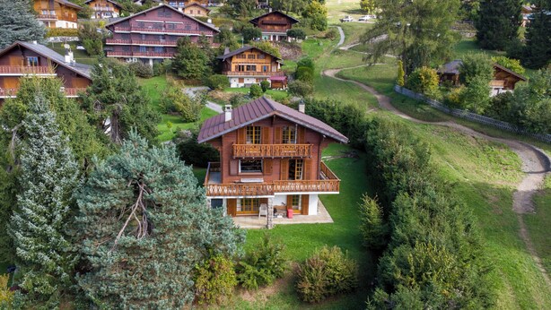 Una cabaña de madera con balcón, rodeada de abundante vegetación y un sendero serpenteante.