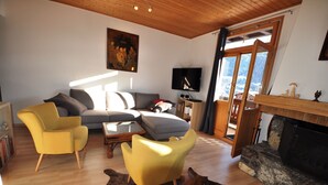 Un salon avec un canapé, deux fauteuils jaunes, un téléviseur et une cheminée.