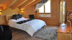 Un dormitorio de cabaña de madera con cama, una silla, un escritorio y una ventana.