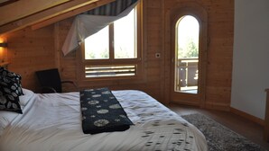 Un dormitorio con una cama grande, una ventana con persianas, techo de madera y un balcón pequeño.