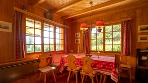 Comedor de madera con una mesa dispuesta para cuatro, ventanas amplias con cortinas y una chimenea.