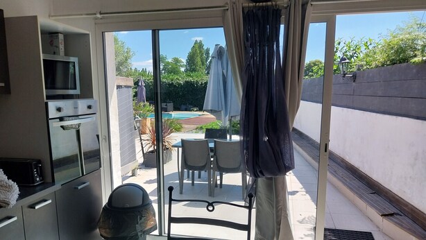 Ett kök med mikrovågsugn, brödrost och kaffebryggare. Det finns en skjutdörr i glas som leder ut till en uteplats med ett bord och stolar, en pool och grönska.