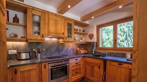 A kitchen with wooden cabinets, a built-in oven, a toaster, and a window with a view of trees.