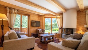 A cozy log cabin interior with a fireplace, comfortable seating, and large windows offering a view of the forest.