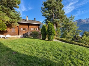 Eine Holzhütte mit einem Steinkamin, umgeben von einem gepflegten Rasen und hohen Bäumen.