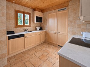 A kitchen with wooden cabinets, a microwave, a sink, and a window with a view of trees. - Chalet Tendre est la Nuit - 3 bedrooms - very pretty and cozy chalet just above the village of Gryon (Gryon)