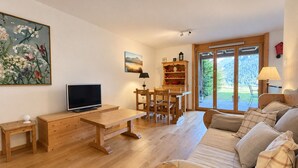 A living room with a wooden sofa, a TV, a wooden table, and a dining area with chairs.