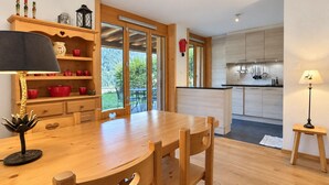 A modern kitchen with wooden cabinets, a dining area with a wooden table and chairs, and a view of the outdoors through large glass doors.