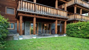 A wooden building with a balcony, stone pillars, and a grassy lawn.
