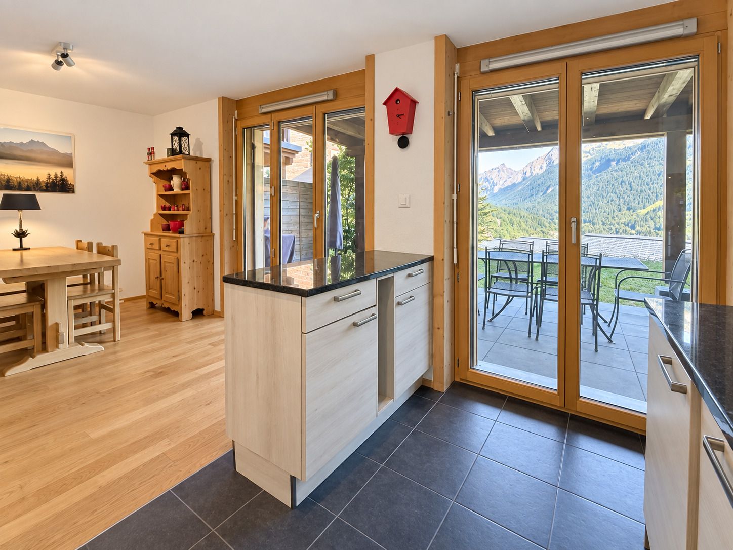 A modern kitchen with a large island, wooden cabinets, and a view of a mountainous landscape through the sliding glass doors.
