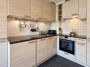 A modern kitchen with light wood cabinets, a black countertop, stainless steel appliances, and a kettle on the counter. - The apartment is located 150m from the Place de la Barboleuse in Gryon and is close to all amenities (Gryon)