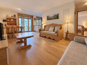 Un salon chaleureux avec un canapé en bois, une table à manger et un coin cuisine doté de meubles en bois et d’une fenêtre.